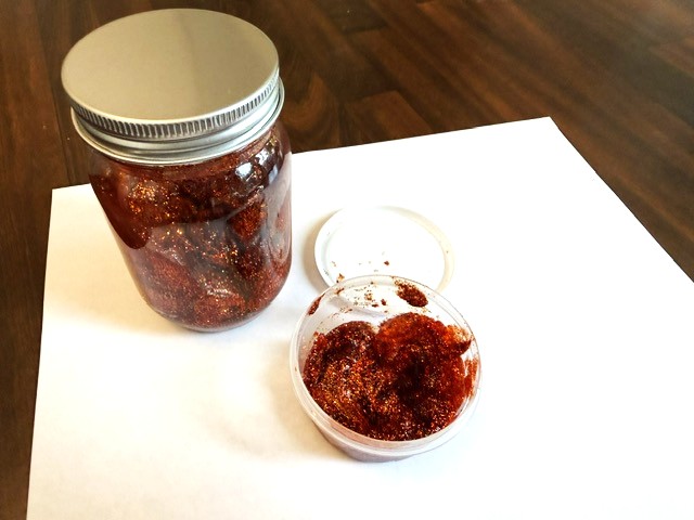 Mason jar of copper-red biodegradable glitter gel with a small application cup beside it